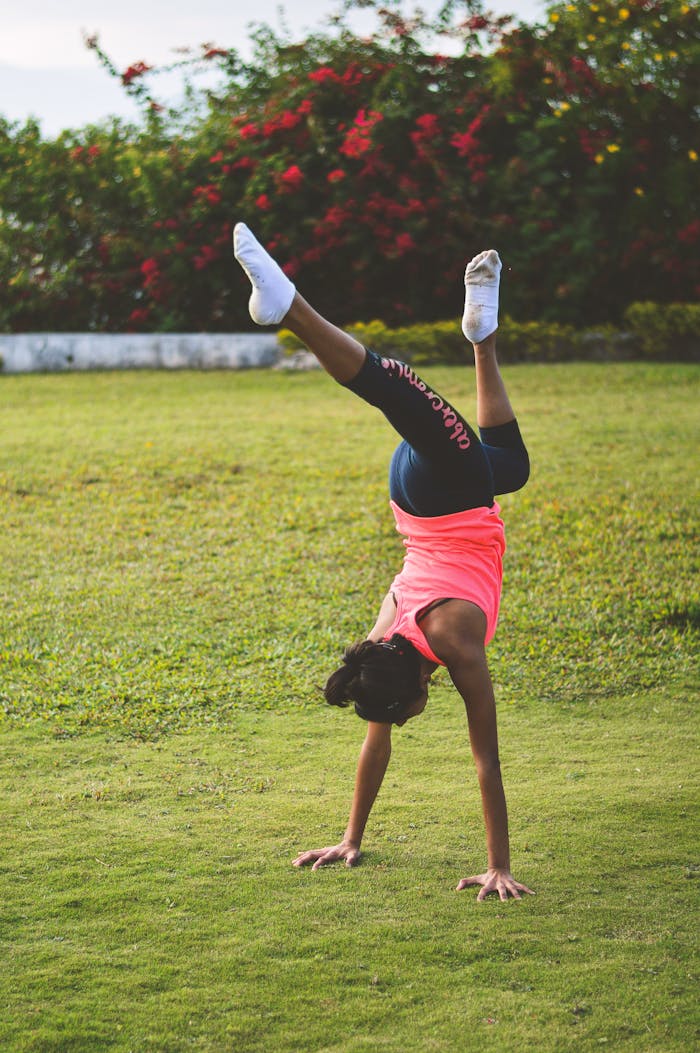Woman in a pink tank top doing a handstand on grass, showcasing outdoor fitness.